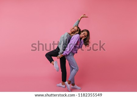 Relaxed fair-haired woman in black pants standing on one leg. Glad slim girl in jeans fooling around with best friend.