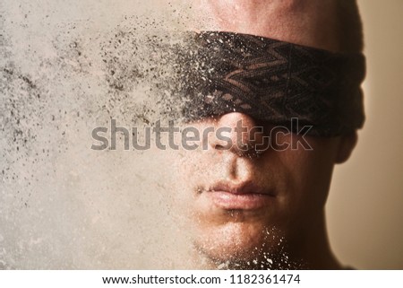 A man with a blindfold over his eyes disintegrates into dust. Royalty-Free Stock Photo #1182361474