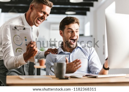 Picture of excited happy emotional men colleagues in office working with computer.