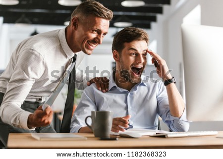 Picture of excited surprised shocked happy emotional men colleagues in office working with computer.