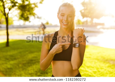 Photo of beautiful young blonde sports woman in park outdoors showing watch clock.