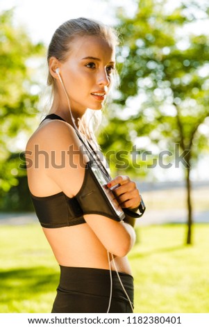 Photo of beautiful young blonde sports woman in park outdoors using mobile phone listening music.
