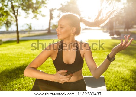 Photo of beautiful young blonde sports woman in park outdoors using mobile phone.
