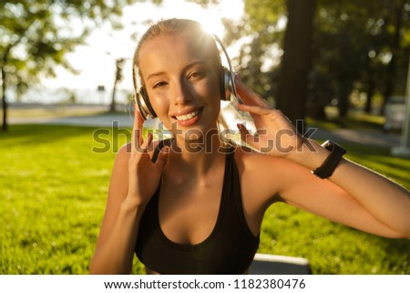 Photo of beautiful young blonde sports woman in park outdoors listening music with headphones.