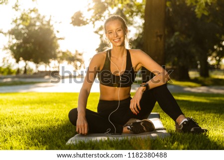 Photo of beautiful young blonde sports woman in park outdoors listening music wth earphones.