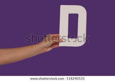 Female hand holding up the uppercase capital letter D isolated against a purple background conceptual of the alphabet, writing, literature and typeface