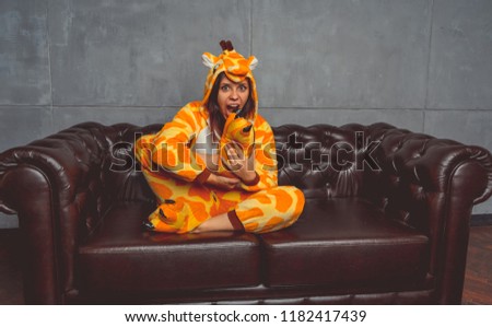 Pajamas in the form of a giraffe. Emotional portrait of a student on the background leather sofa. 