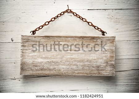 aged wood signboard hanging on white wall with rusty chain