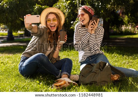 Two happy young girls friends having fun at the park, taking a selfie, having a picnic