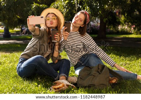 Two pretty young girls friends having fun at the park, taking a selfie, having a picnic