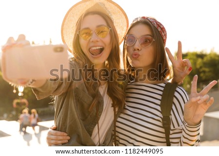 Two lovely young girls friends having fun together, taking a selfie at the city