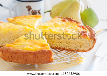 Pie from the cottage cheese pastry with pear and sour cream, cut into pieces on a white table, horizontal