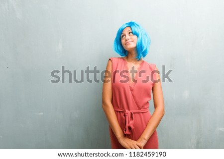 Portrait of young elegant blonde woman looking up, thinking of something fun and having an idea, concept of imagination, happy and excited. She is wearing a blue wig.