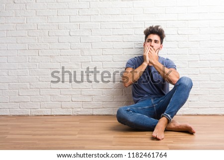 Young natural man sit on a wooden floor covering mouth, symbol of silence and repression, trying not to say anything