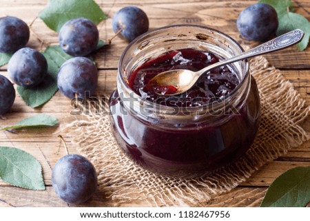 Plum jam in a glass jar. Fresh plum fruit on a wooden table