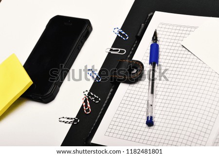 Office tools and mobile phone on black and white background. Business and work concept. Blank cards, pen, paper clips and organizer, top view.  Leather covered notebook opposite gadget.
