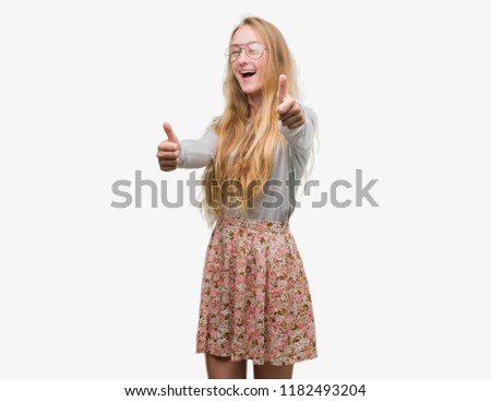 Blonde teenager woman wearing flowers skirt approving doing positive gesture with hand, thumbs up smiling and happy for success. Looking at the camera, winner gesture.