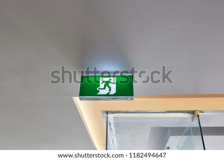 Fire exit sign hanging overhead on ceiling for security protection in building. Selective focus