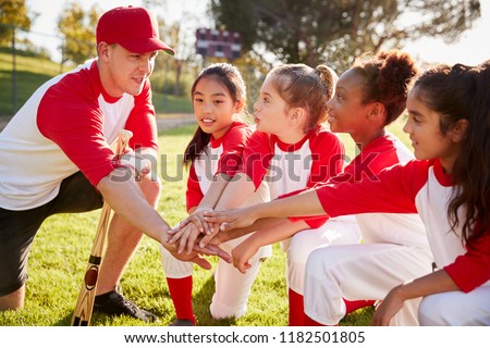 Girl baseball team kneeling with their coach, touching hands