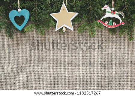 Christmas card with place for your text and design. A beautifully framed frame on top of green branches of a Christmas tree and wooden figures of fir, a star and a horse. Background from canvas