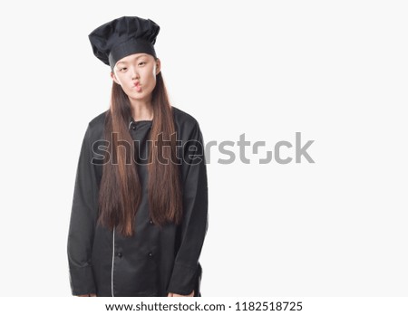 Young Chinese woman over isolated background wearing chef uniform making fish face with lips, crazy and comical gesture. Funny expression.