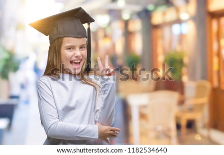 Young beautiful girl wearing graduate cap over isolated background smiling with happy face winking at the camera doing victory sign. Number two.
