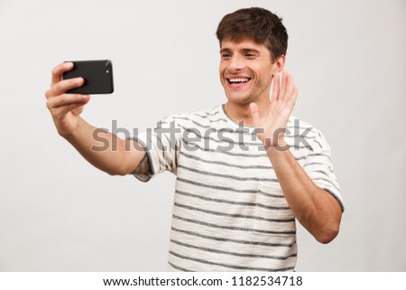 Portrait of a cheerful young man standing isolated over white background, taking selfie with mobile phone