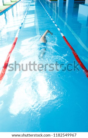 Image of young sporty man in blue cap swimming on back in swimming pool