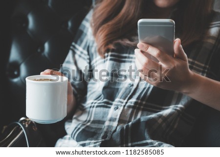 Closeup image of a woman holding , using and touching a smart phone while drinking coffee