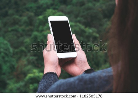Mockup image of a woman holding white smart phone with blank desktop screen in outdoor with blur green mountains background