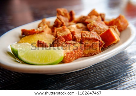Colombian fried pork belly, chicharrón colombiano, with sliced limes Royalty-Free Stock Photo #1182647467