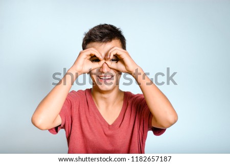 young man shows binoculars with hands, isolated studio photo on background