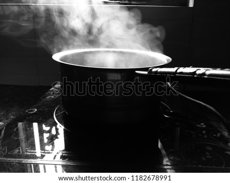 Tea making utensil with steam above electric induction stove in black and white colour picture.