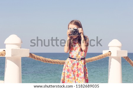 A girl photographs with a camera in a red dress against the sea. Toning