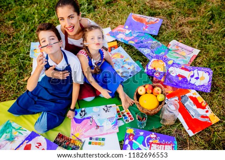 Happy mother, and two kids are painting in the park. The concept of a happy family.