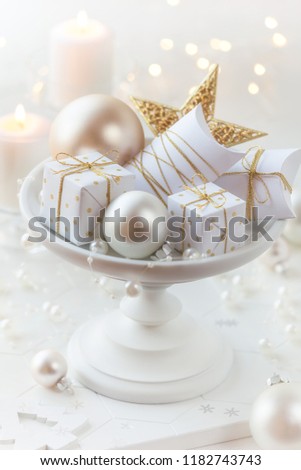 White Christmas gifts with golden ribbons on a stand with festive Xmas decorations and baubles