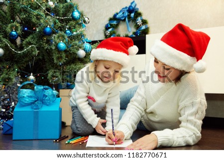 happy mother and little daughter writing a letter to Santa Claus near Christmas tree. New Year and xmas people