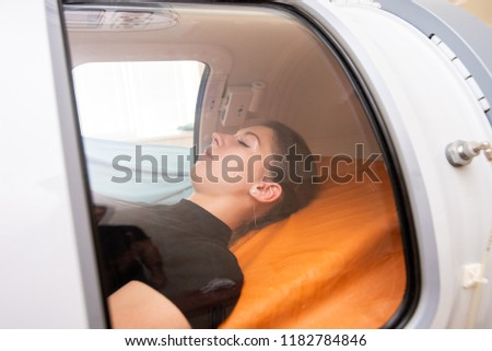 beautiful girl in a black T-shirt and white pants lies in a hyperbaric chamber Royalty-Free Stock Photo #1182784846