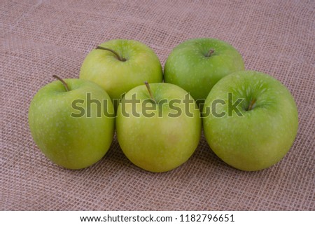 Five green granny smith apples on burlap surface. View from above.