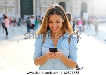 Happy casual woman wearing shirt texting on the smart phone walking in the street in a sunny day