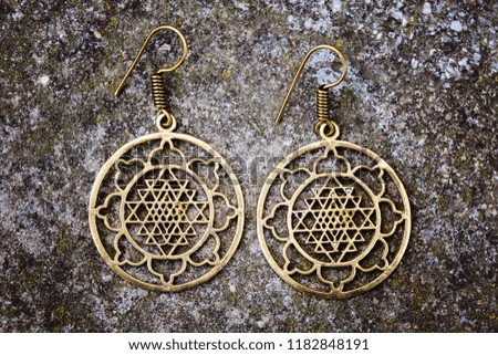 Indian spiritual ornamental style brass earrings on rocky background