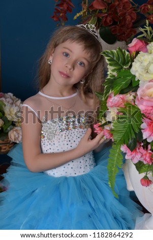 girl in white with blue festive dress next to bouquets of flowers