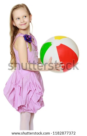 Happy little blond girl, with long curly hair, in a beautiful pink dress above the knees.She plays with a large multi-colored inflatable ball.
