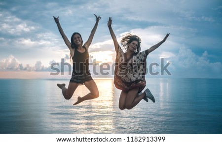 Two happy girls jumping at sunset on tropical beach. Koh Tao, Thailand