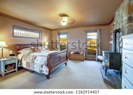 Master bedroom interior with wooden sleigh bed, old wood burning stove and river rock wall. Northwest, USA