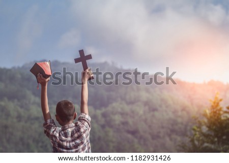 Boy holding holy Bible and christian cross with light sunset background. young christian concept