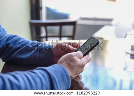 Man sitting at restaurant table checking cellphone - hands only