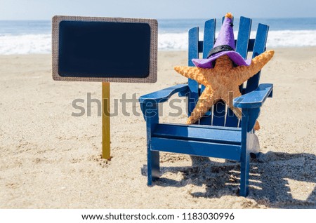 Halloween background with starfishes in the witch's hats and black board on the sandy beach near the ocean 