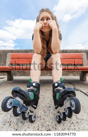 Sad funny teenage woman wearing roller skates. Frustrated female waiting for somebody while sitting on bench outdoor.