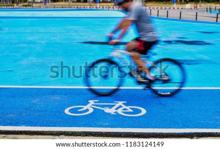 Bicycle lane signs on the bicycle way with blue colored asphalt. Male cyclist rides a bike on the lane of bicycle sign.